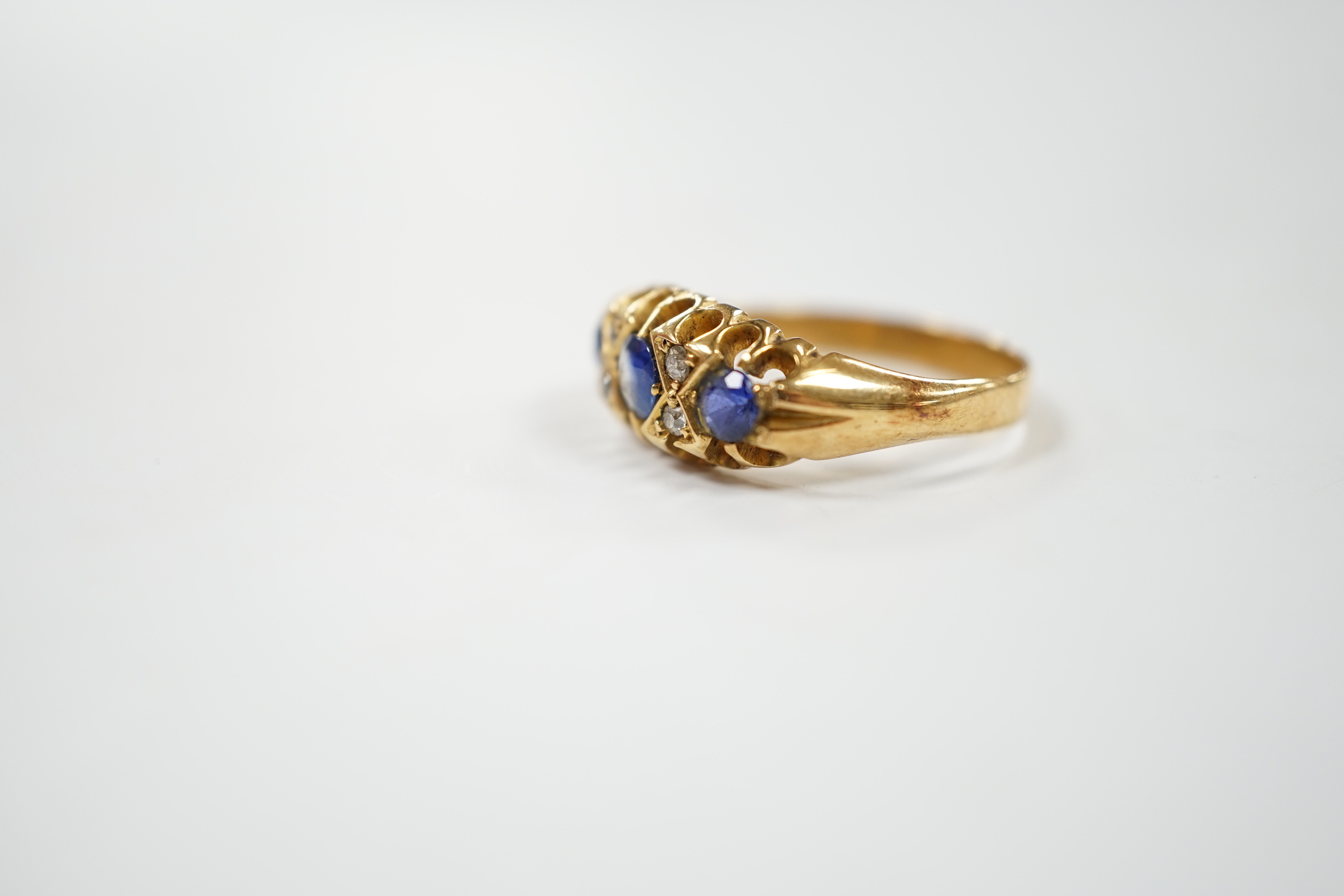 An early 20th century yellow metal, three stone sapphire and four stone diamond chip set half hoop ring, size P, gross weight 4.7 grams.
